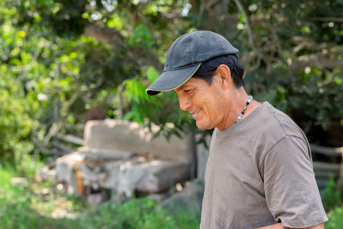 Mature adult man with a cap smiling while working outdoors, representing farming, labor, and rural life